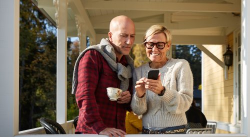 Illustrasjonsfoto av et ektepar som står på balkongen og ser på en telefon sammen