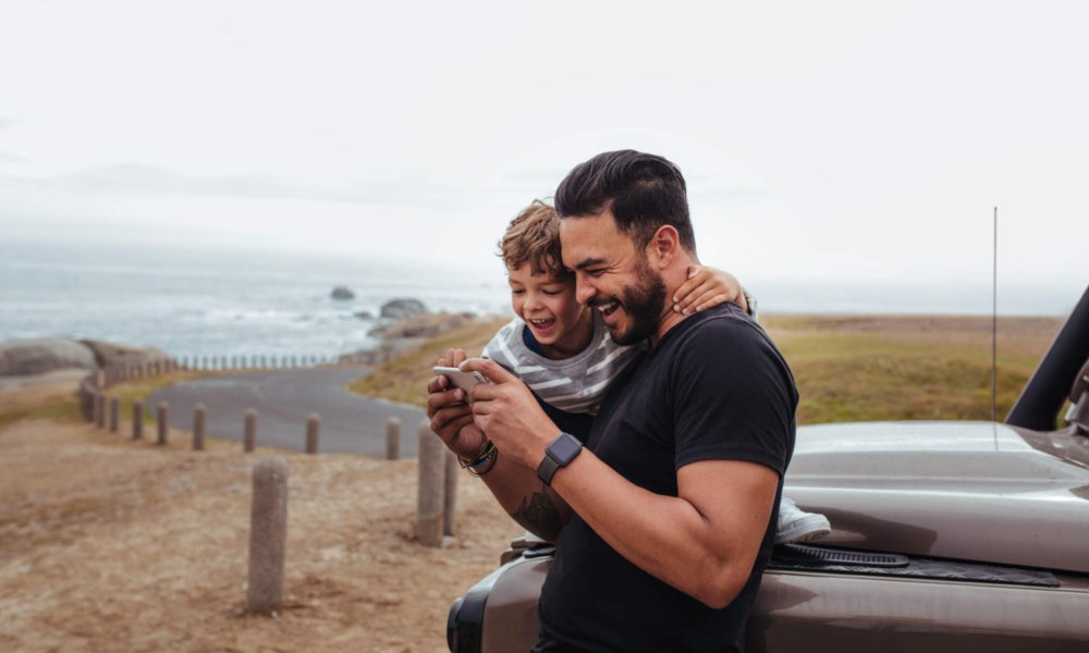 Illustrasjonsfoto: Far med barn som ser på en mobil og smiler.
