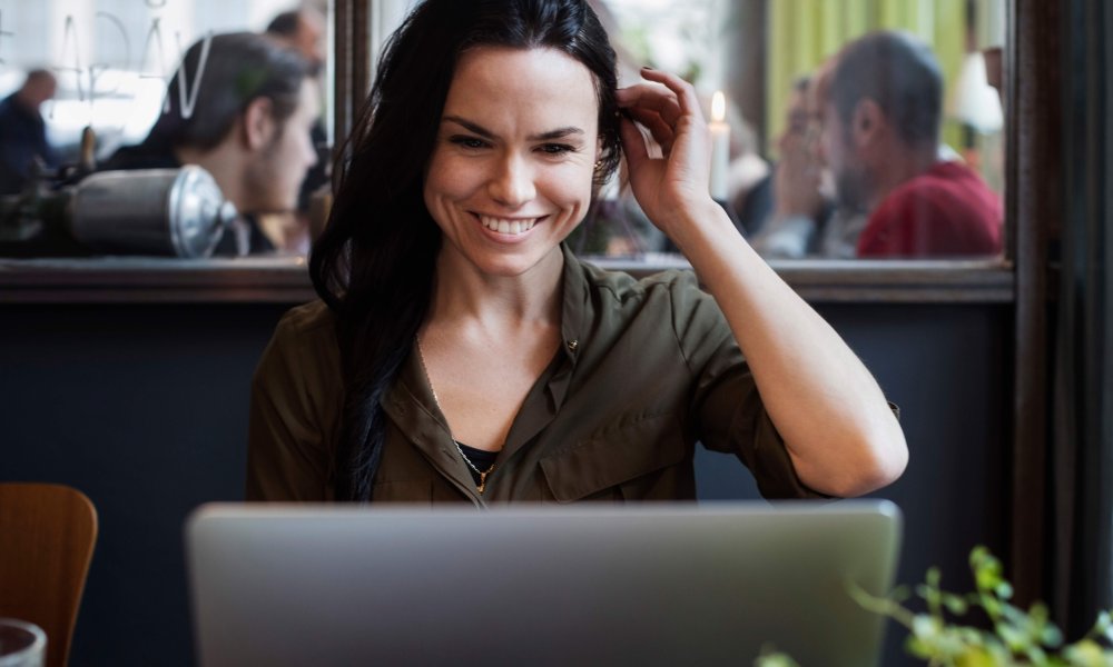 Illustrasjonsfoto: Smilende kvinne foran pc på kafe.