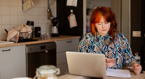 Illustrasjonsfoto: dame med laptop og mobil ved kjøkkenbordet.