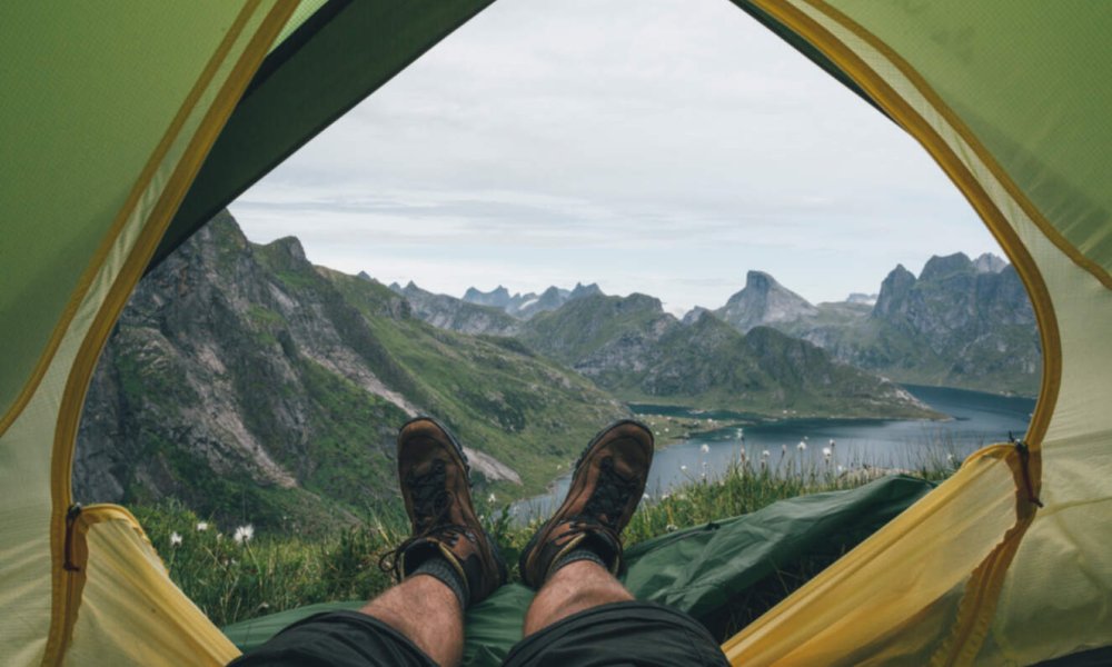 Illustrasjonsfoto: Et par bein stikker ut av et telt på fjellet med fantastisk utsikt.