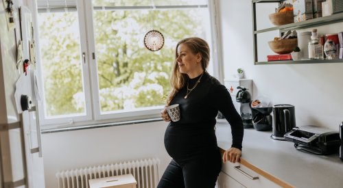 Illustrasjonsfoto: En gravid kvinne lener seg mot kjøkkenbenken med en kopp i hånden.